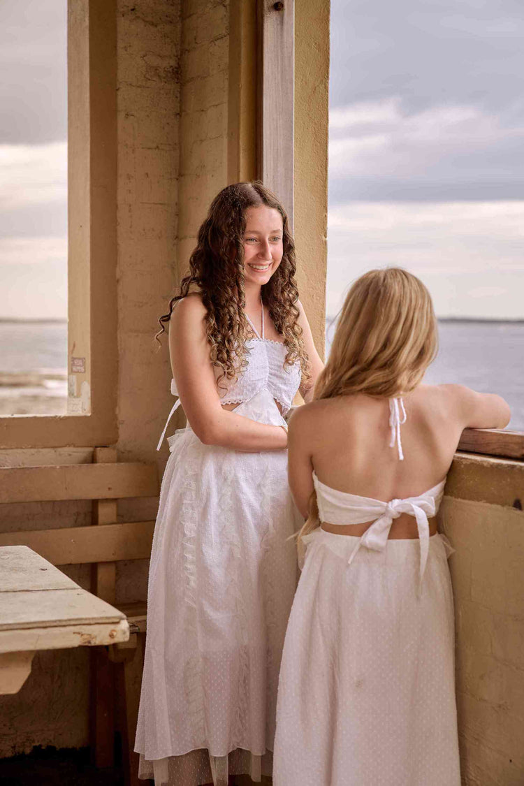 Two tween girls in white dresses standing by a window